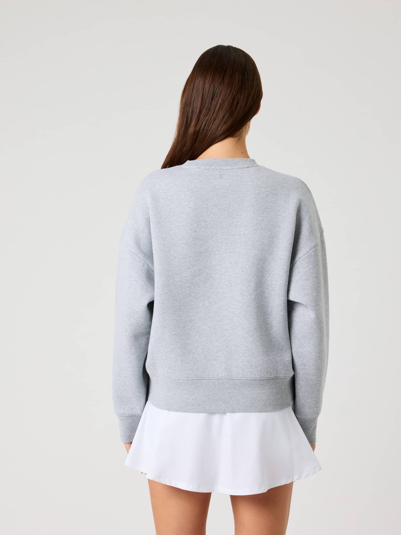 Back view of a woman wearing the oversized Borg Boyfriend Sweatshirt in Light Grey Melange (Grey) and a white skirt. - Image 3