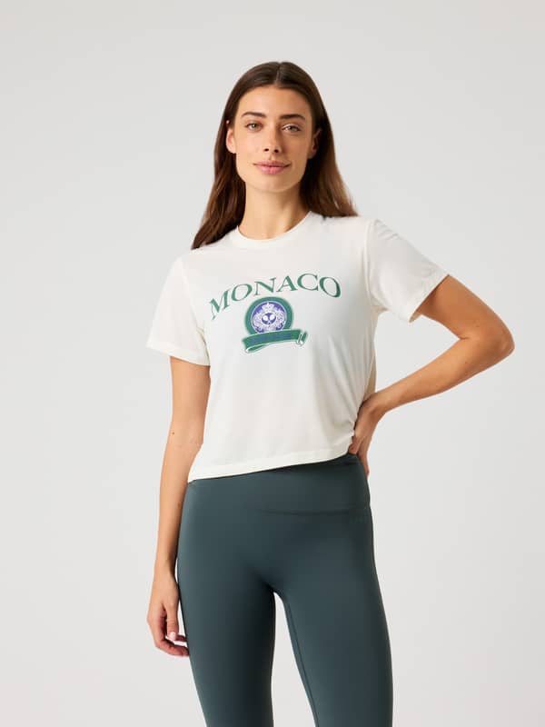 Front view of a woman wearing the Tofu (White) Borg Cropped T-Shirt with a green Monaco tennis graphic for training.