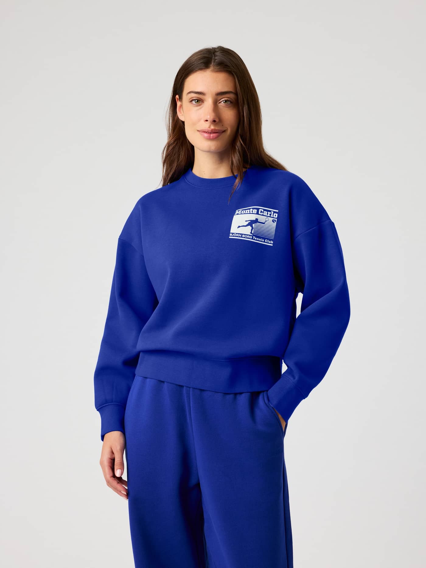 Vorderansicht einer Frau im Clematis Blue (Blau) Borg Boyfriend Sweatshirt mit oversized Passform und weißem Tennis-Logo. - Image 2