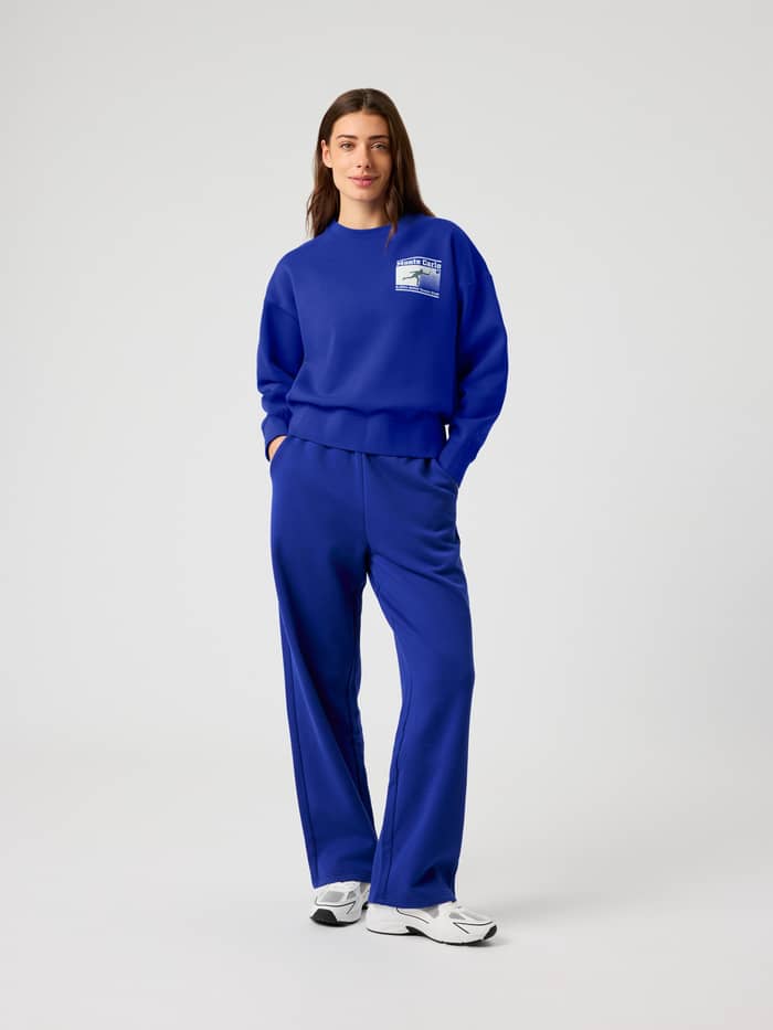 Ganzkörper-Vorderansicht einer Frau im oversized Borg Boyfriend Sweatshirt in Clematis Blue (Blau) mit Tennis-Logo. - Image 5