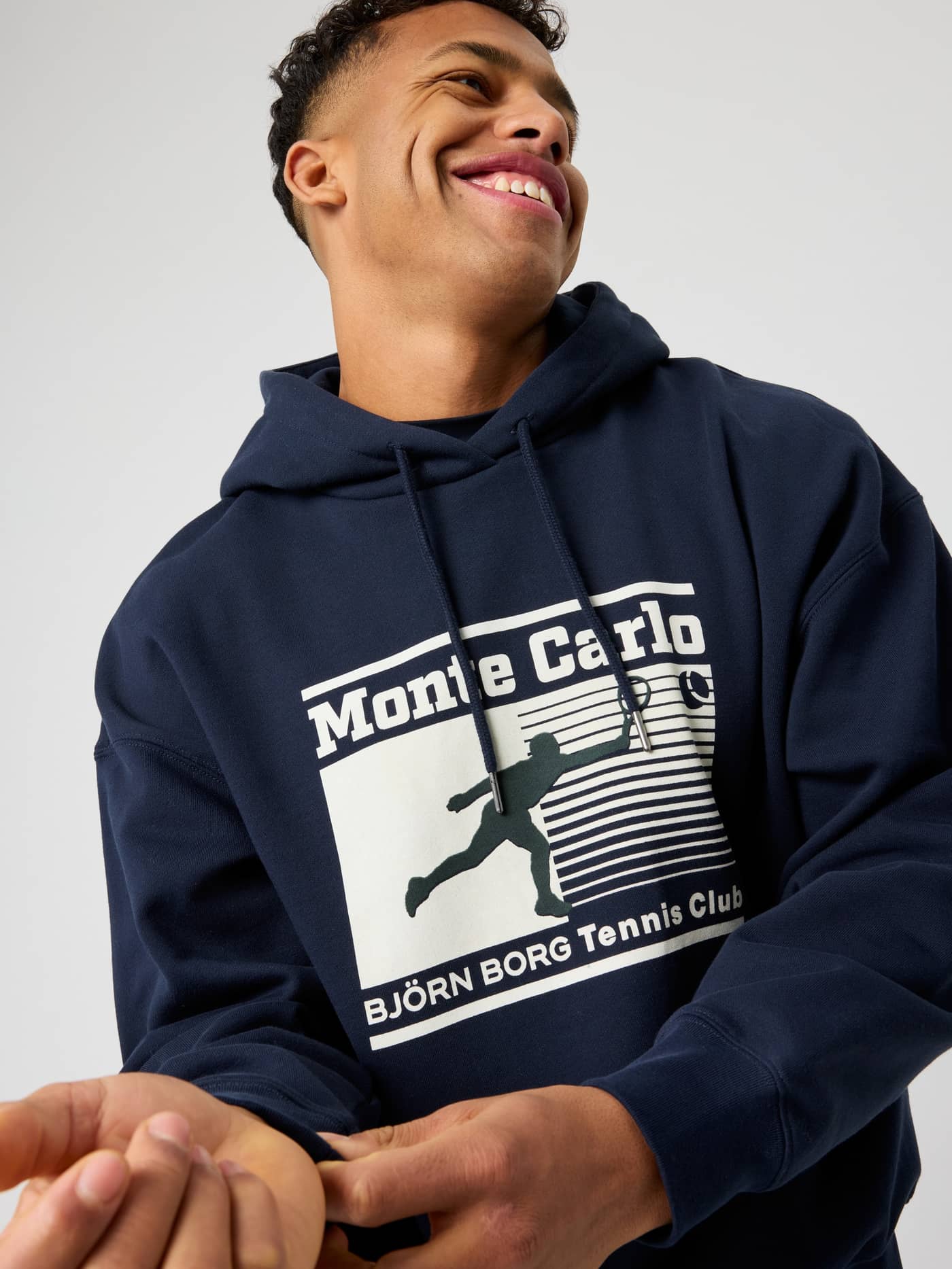 Närbild på en man i Borg Oversized Hoodie i Night sky (Marinblå) med snygg tennis club-grafik. - Image 1