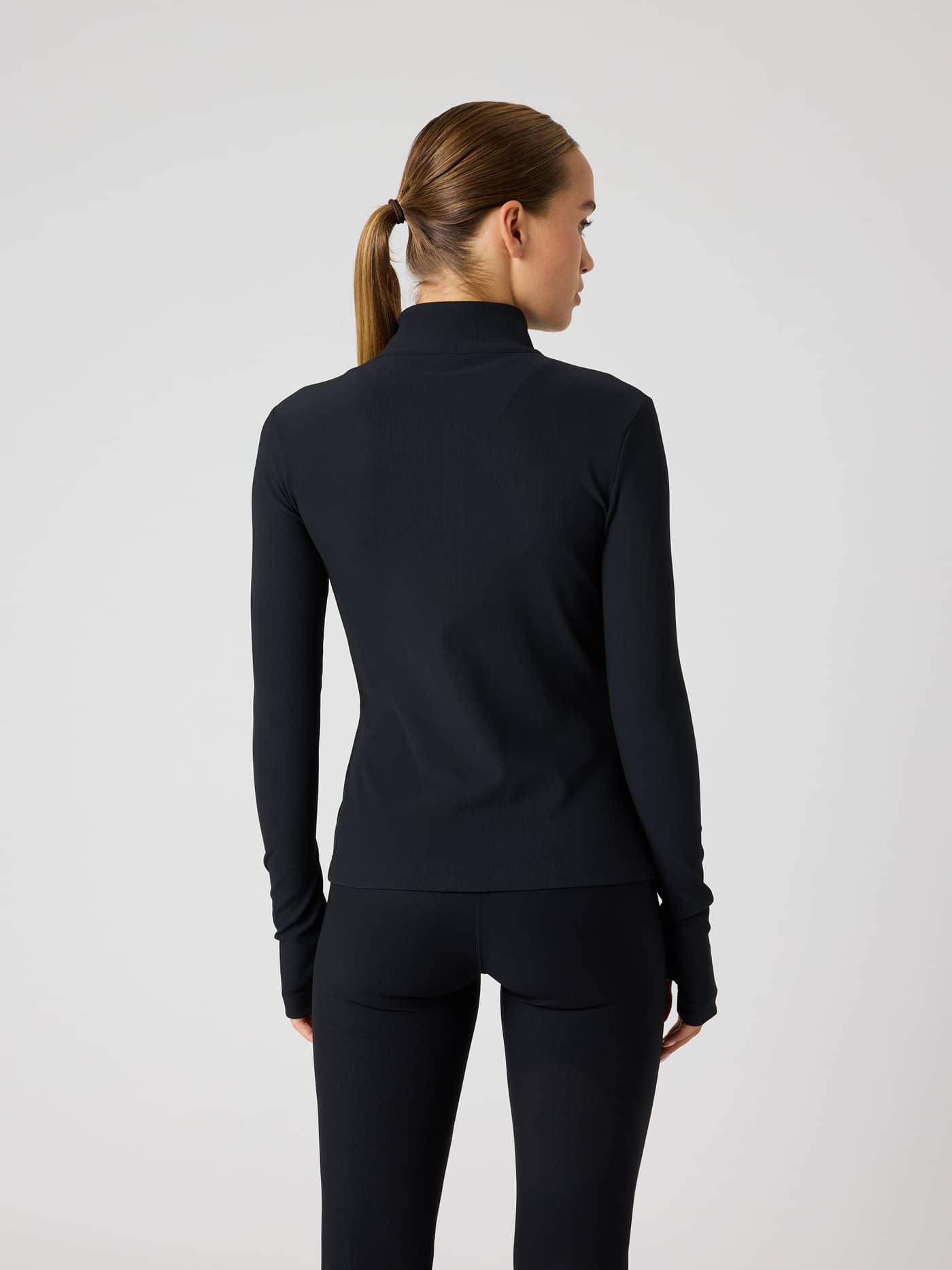 Back view of a woman wearing the Studio Premium Ribbed Midlayer in Black Beauty (Black), highlighting a sleek training fit. - Image 3
