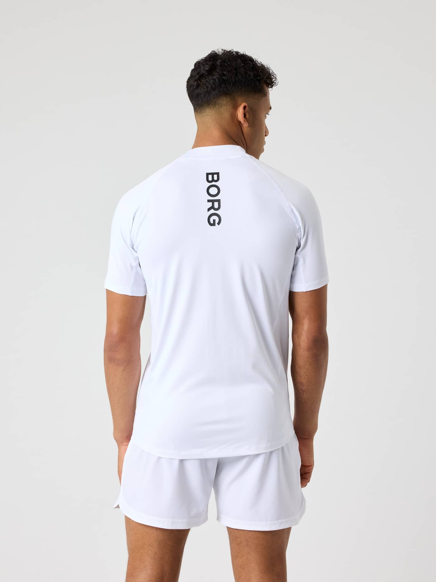 Back view of a man wearing the Brilliant White (White) Borg Mock Neck T-Shirt with a vertical black logo for tennis training. - Image 2