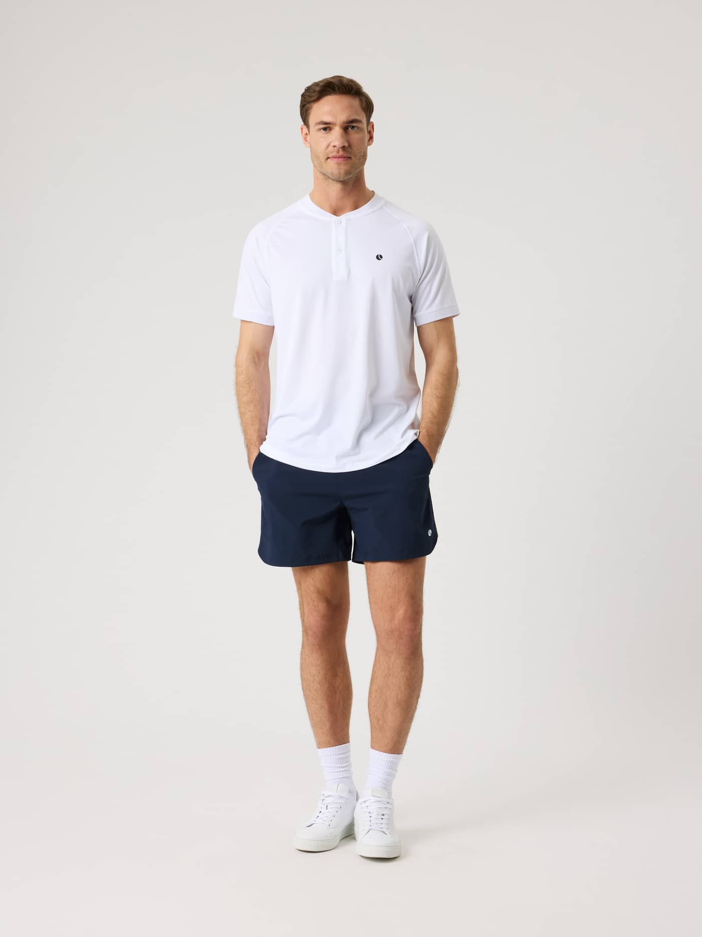 Full-body front view of a man in the Brilliant White (White) Ace Sports Polo Shirt for tennis with a black logo. - Image 3