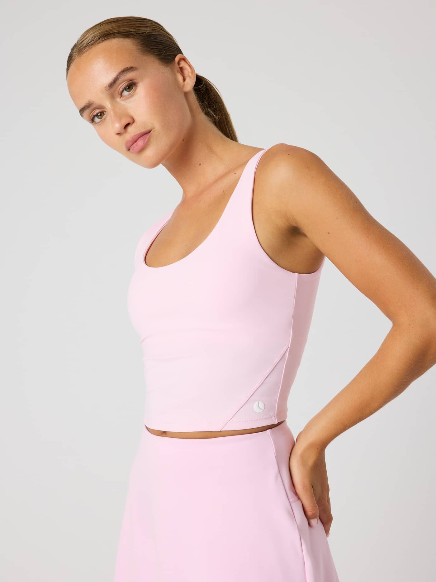 Vue latérale d'une femme en Ace 2 In 1 Cropped Tank à coupe ajustée Pink Lady (Rose) avec logo de balle de tennis blanc. - Image 4
