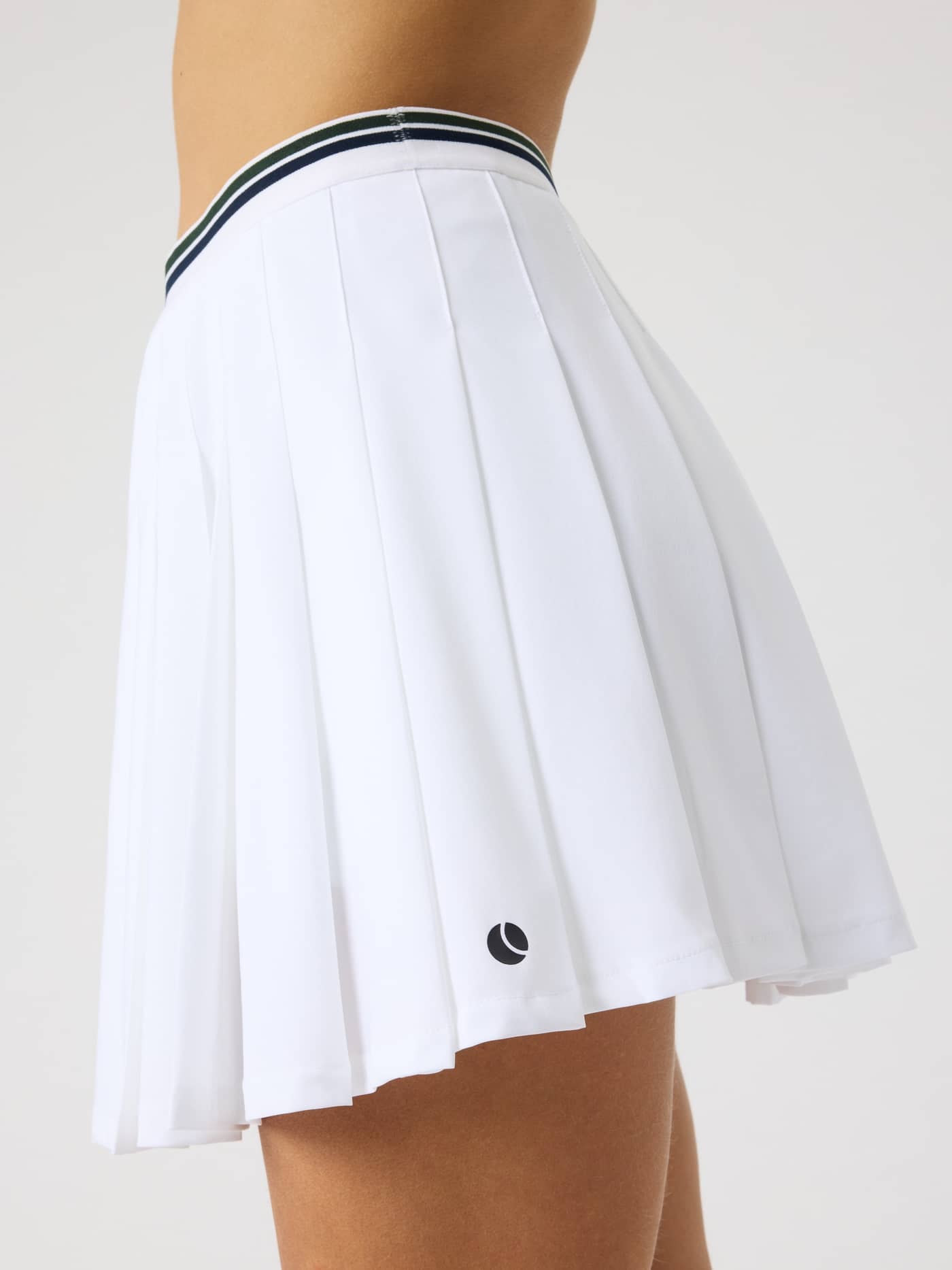 Side view of the Ace Pleated Skirt in Brilliant White (White) featuring a pleated style for tennis and a black logo. - Image 6