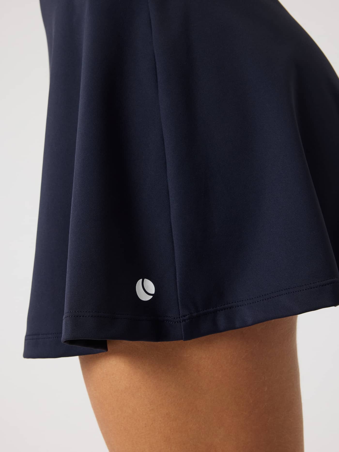 Close-up of the Ace Court Skirt in Night sky (Navy) featuring a white tennis logo and high-stretch performance fit. - Image 4