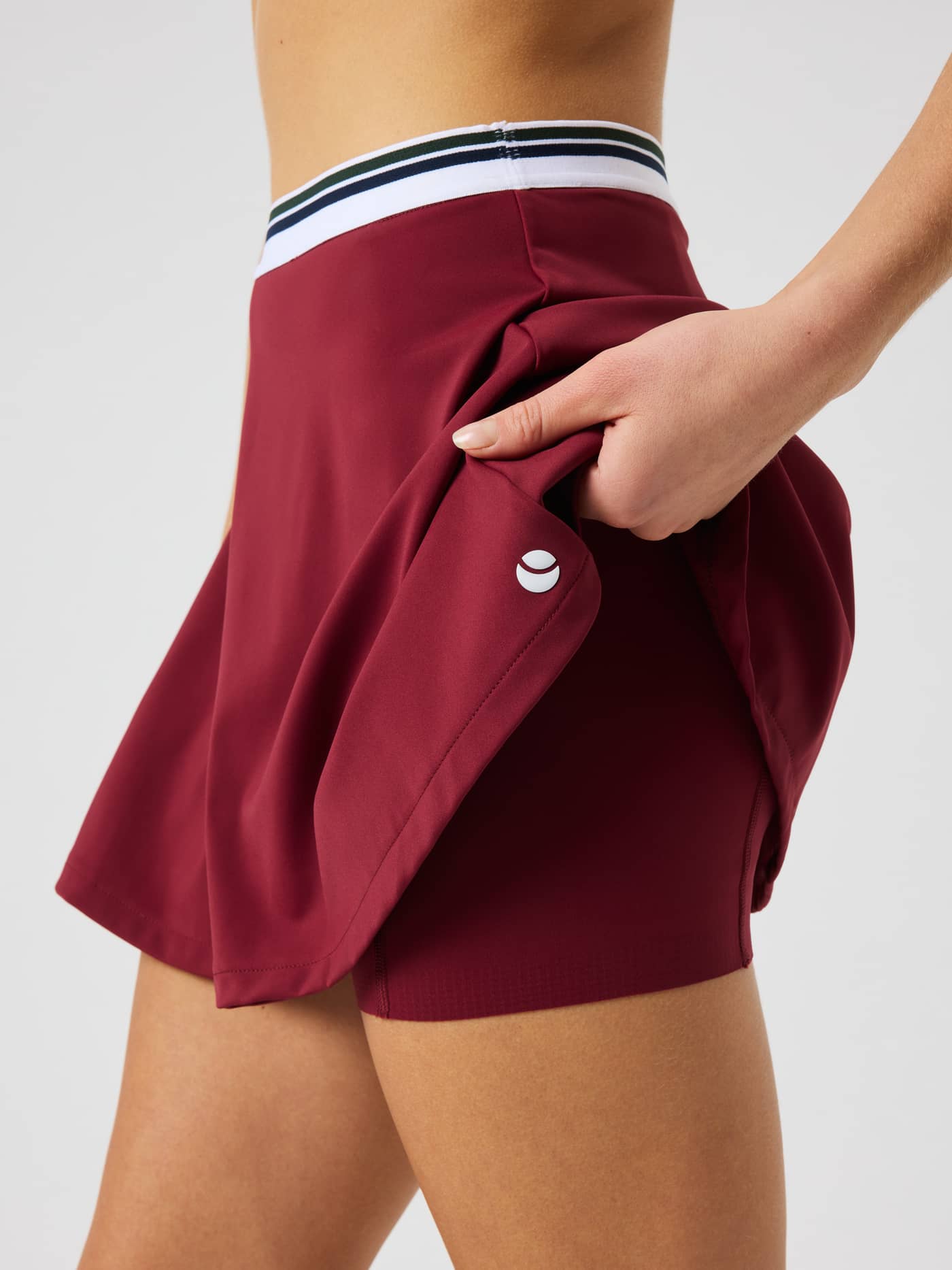 Close-up of the Ace Court Skirt in Cabernet (Red) highlighting the integrated inner shorts and tennis functionality. - Image 5