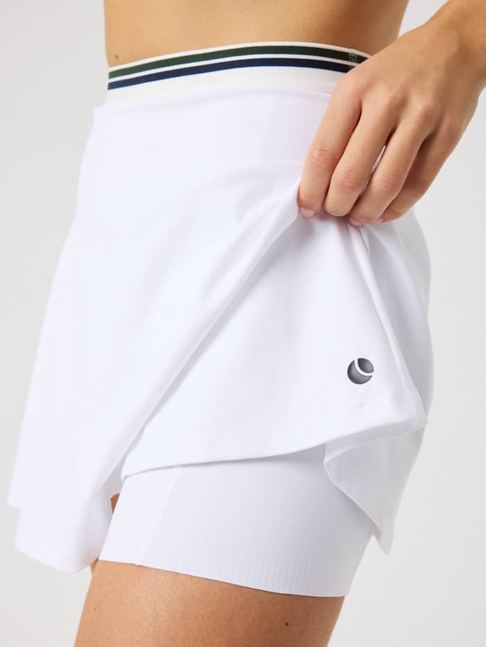 Zijaanzicht van de Ace Court Skirt in Brilliant White (Wit) met zwart logo en geïntegreerde binnenbroek voor tennis. - Image 4