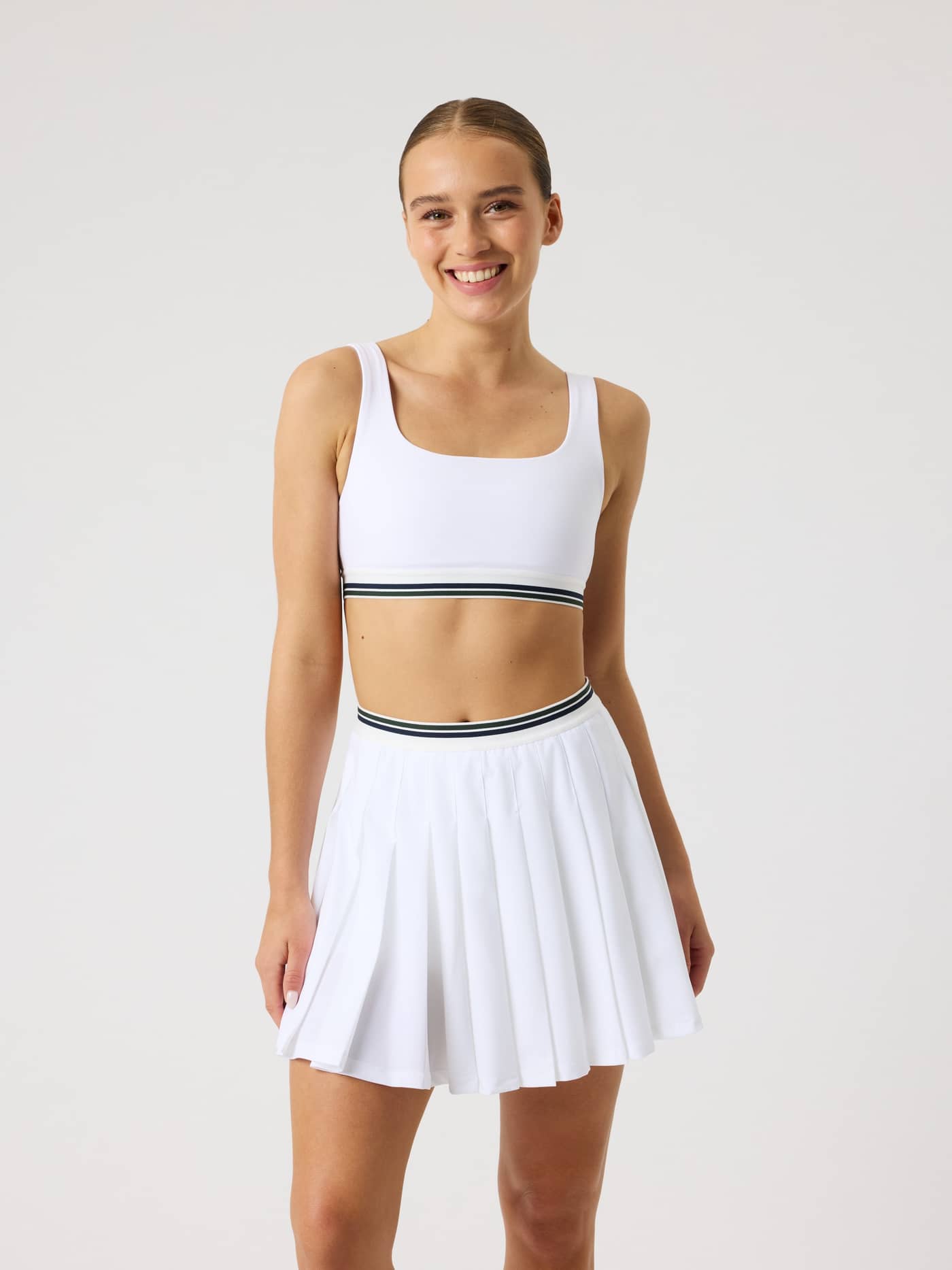 Front view of a model in the Ace Court Top in Brilliant White (White), a performance tennis top with a striped waistband. - Image 2