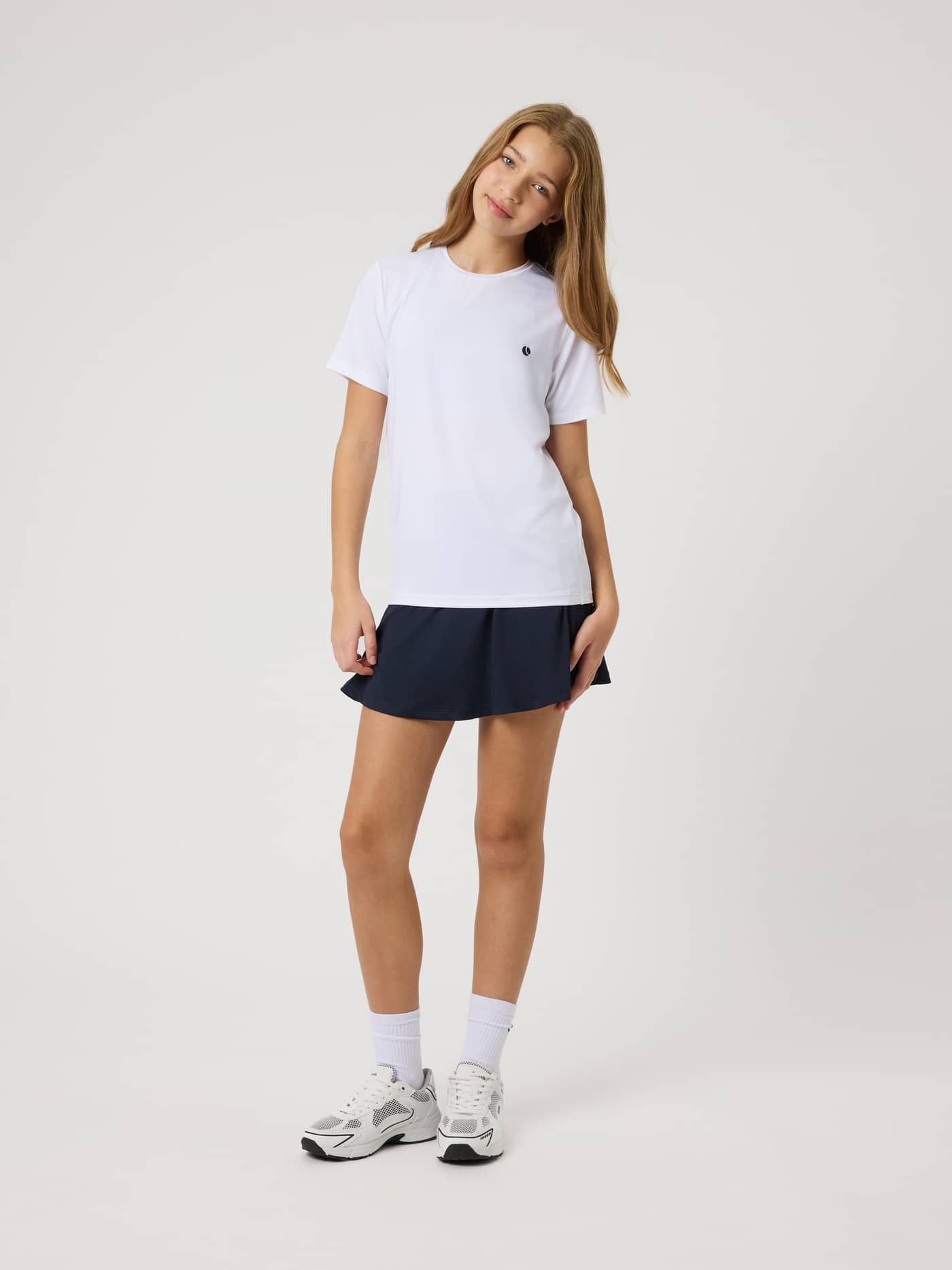 Full-length view of a model in the kids Ace Jersey Skirt in Night Sky (Navy), a flexible tennis skirt. - Image 3