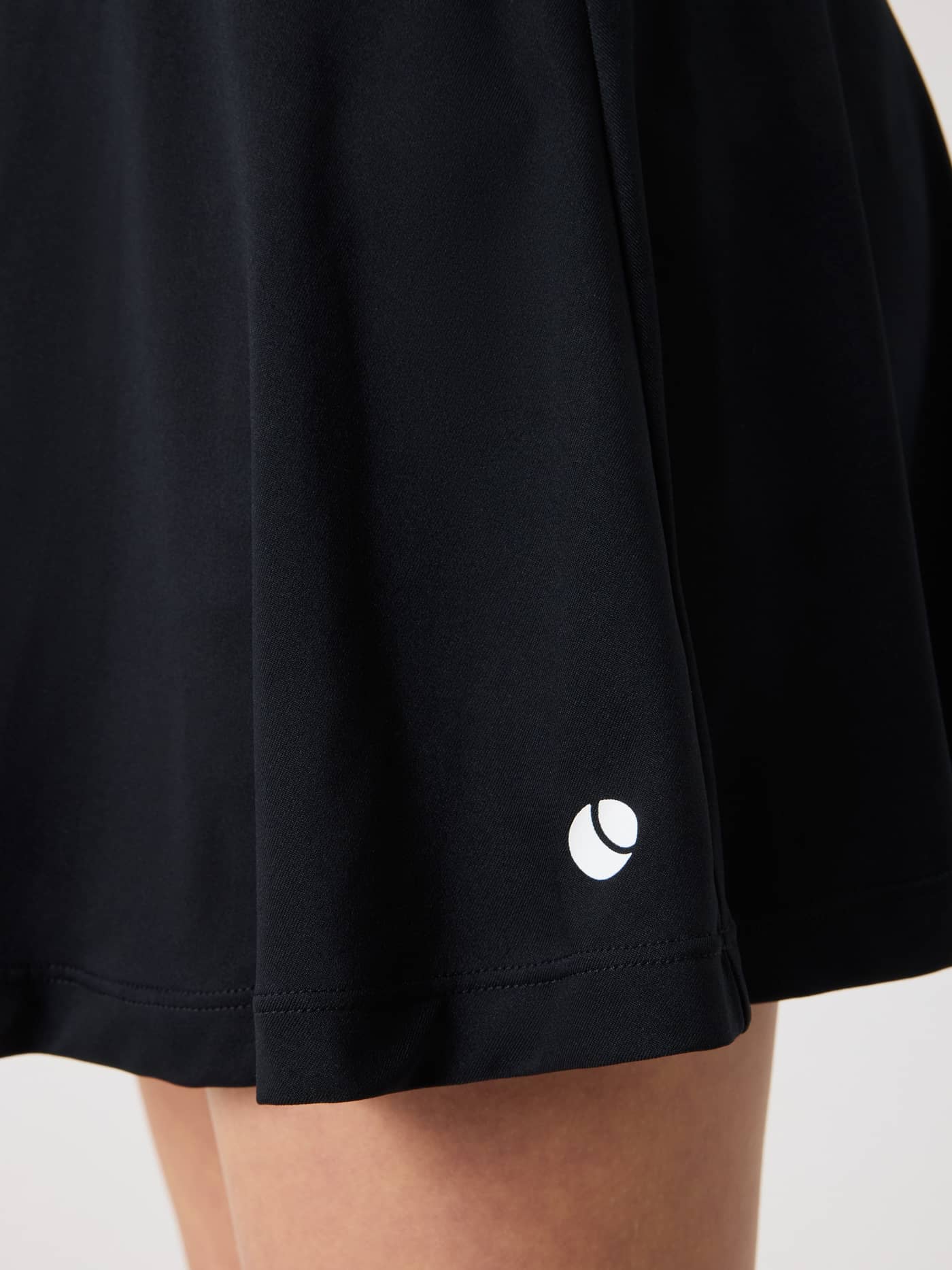 Detailed close-up of the kids Ace Jersey Skirt in Black Beauty (Black), highlighting the white tennis logo on the hem. - Image 4