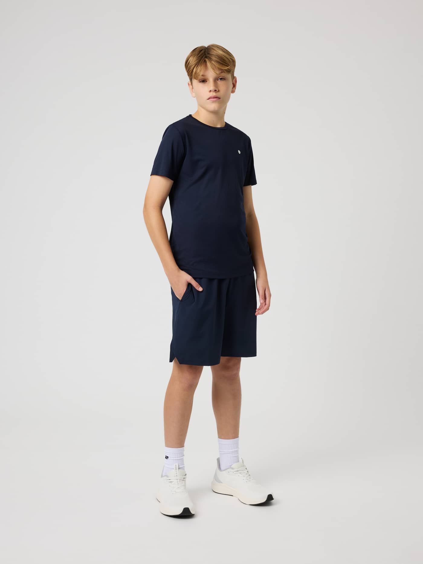 Full-body front view of a kid in the Ace Light T-Shirt in Night sky (Navy) with a white logo for kids tennis and training. - Image 3