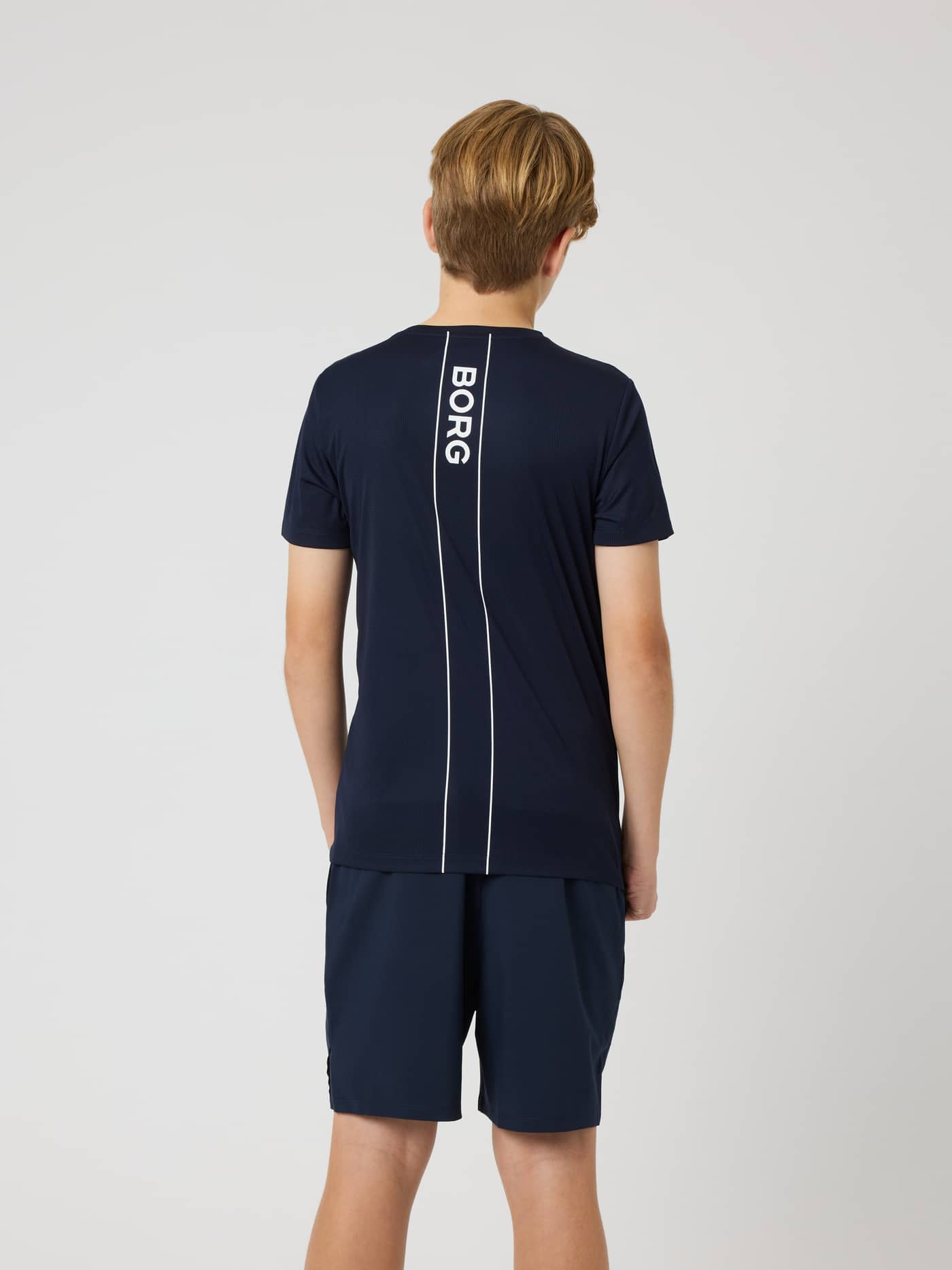 Back view of kids wearing the Ace Light T-Shirt in Night sky (Navy) with a white Borg stripe logo, designed for tennis. - Image 2
