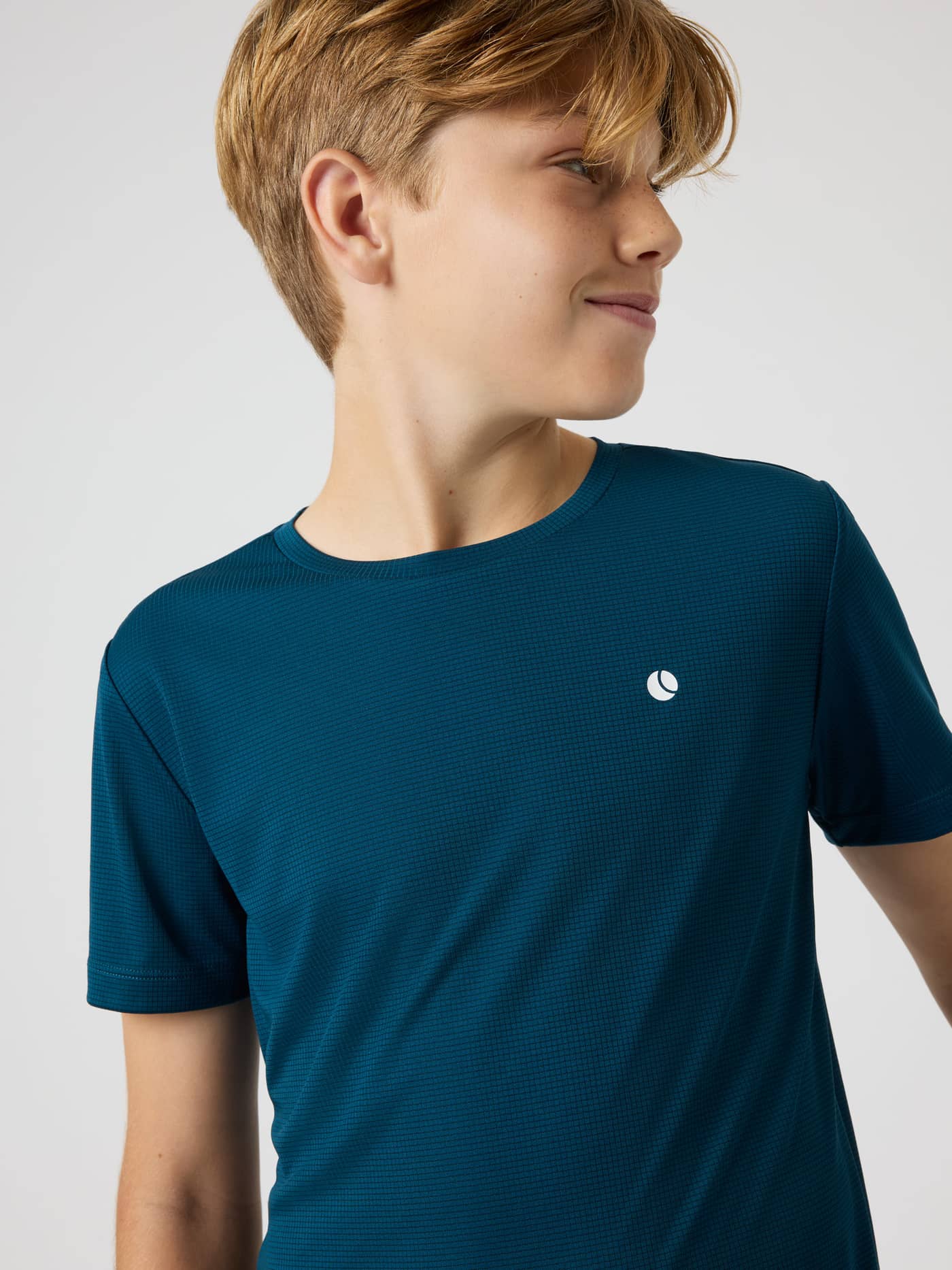 Close-up of a kid wearing the Ace Light T-Shirt in Reflecting Pond (Green), a breathable mesh top for tennis training. - Image 4