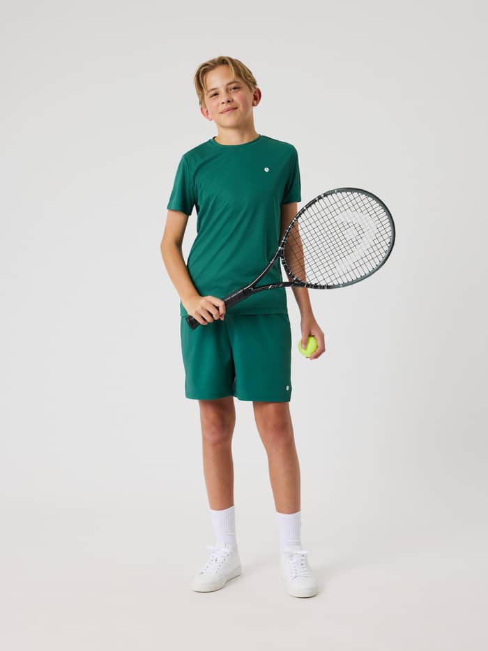 Björn Borg Ace Racquet Shorts för kids i Posy Green (Grön) sedd framifrån i helfigur med tennisracket för träning.