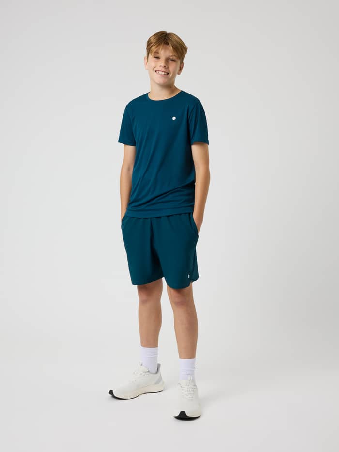 Ace Racquet Shorts in Reflecting Pond (Green) on a boy, featuring a white logo for kids' tennis and padel.