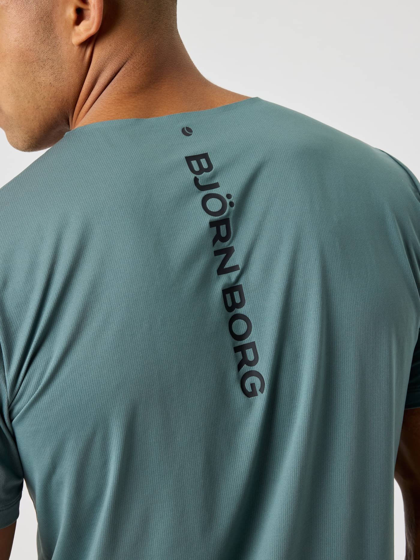 Close-up van het Balsam Green (Groen) Borg Feather T-Shirt met zwart verticaal logo en tennisbalprint voor training. - Image 4