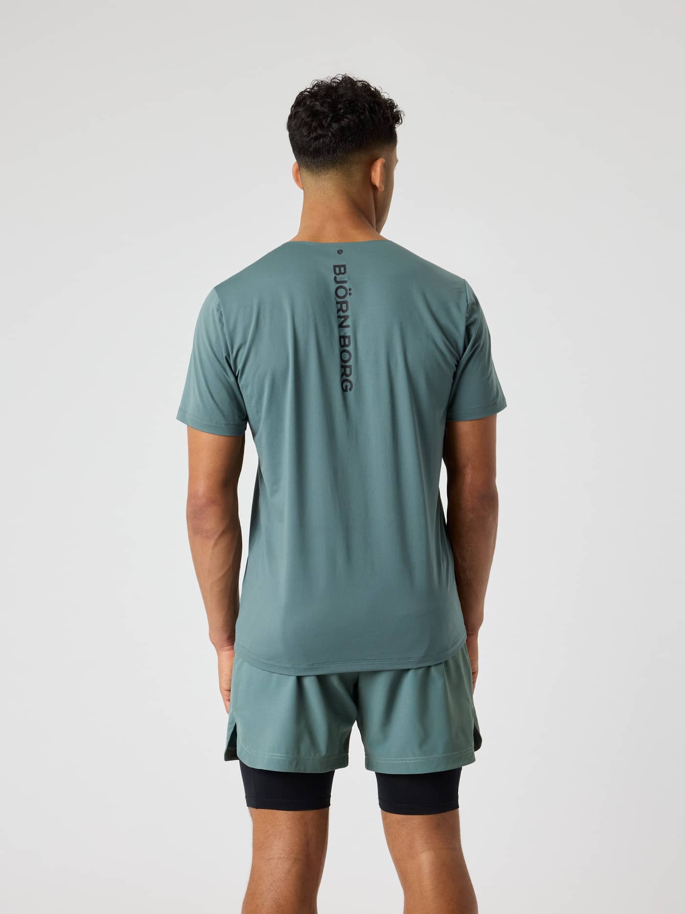 Achteraanzicht van een man in het Balsam Green (Groen) Borg Feather T-Shirt voor training en tennis met een zwart logo. - Image 2