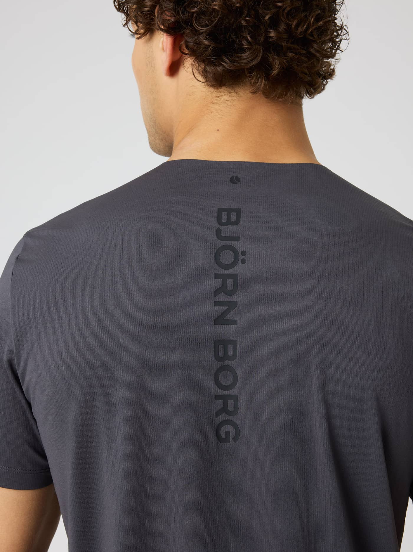 Back view of the Borg Feather T-Shirt in Asphalt (Grey) featuring a vertical logo for training and tennis sessions. - Image 5