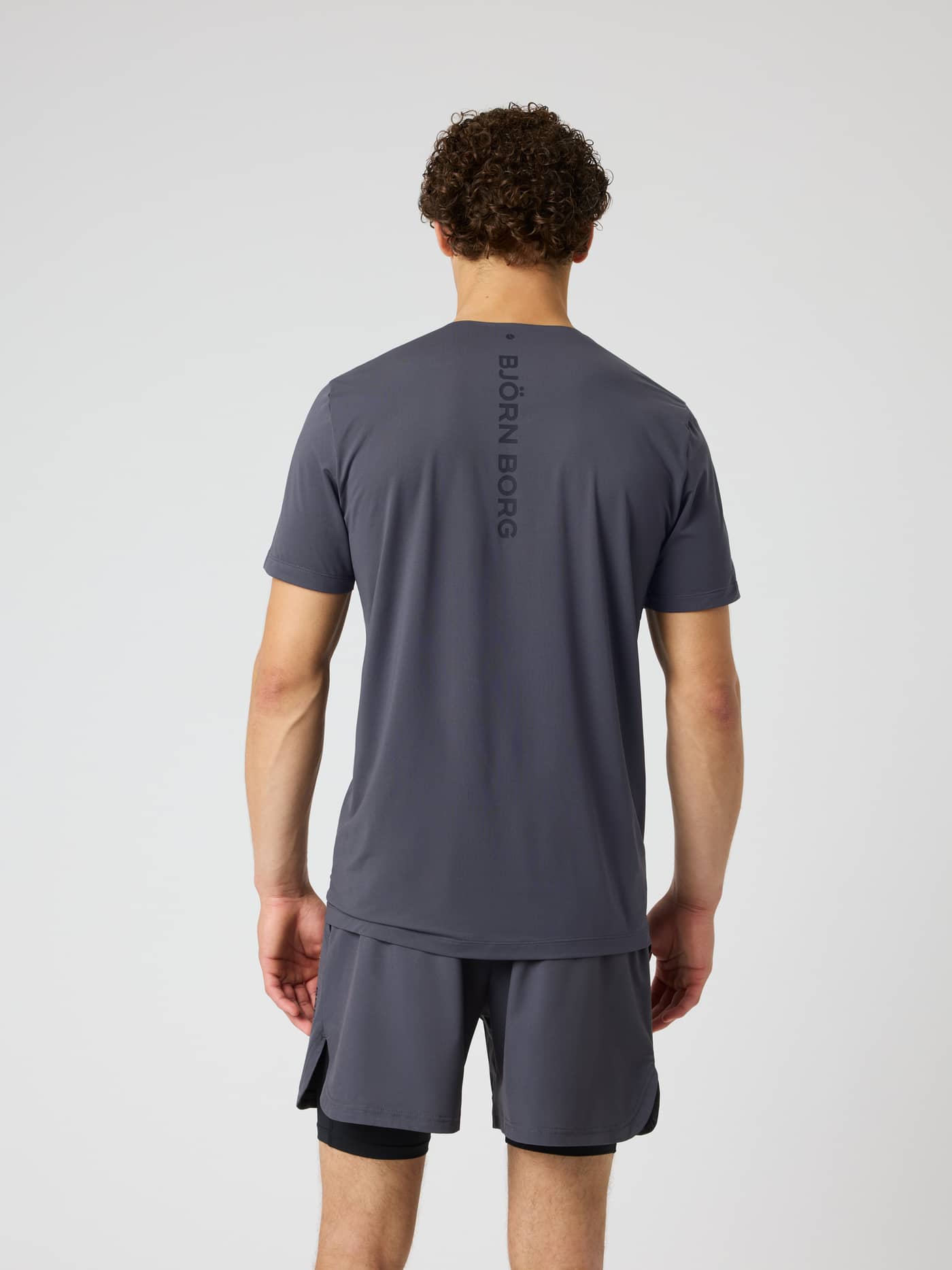 Back view of a model wearing the Borg Feather T-Shirt in Asphalt (Grey) with a vertical logo for training and tennis. - Image 2