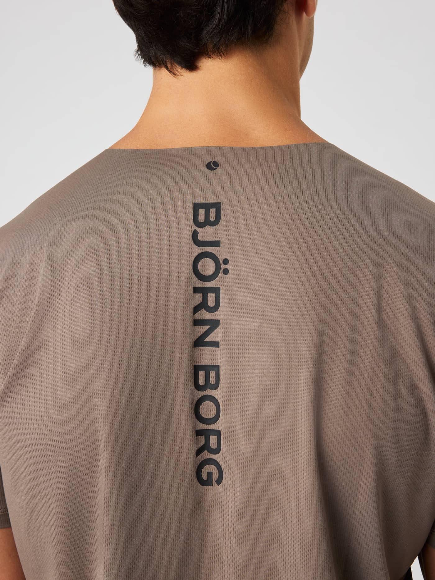 Borg Feather T-Shirt i Falcon (Brun) set bagfra i nærbillede med sort vertikalt logo og tennisbold-detalje til træning. - Image 4