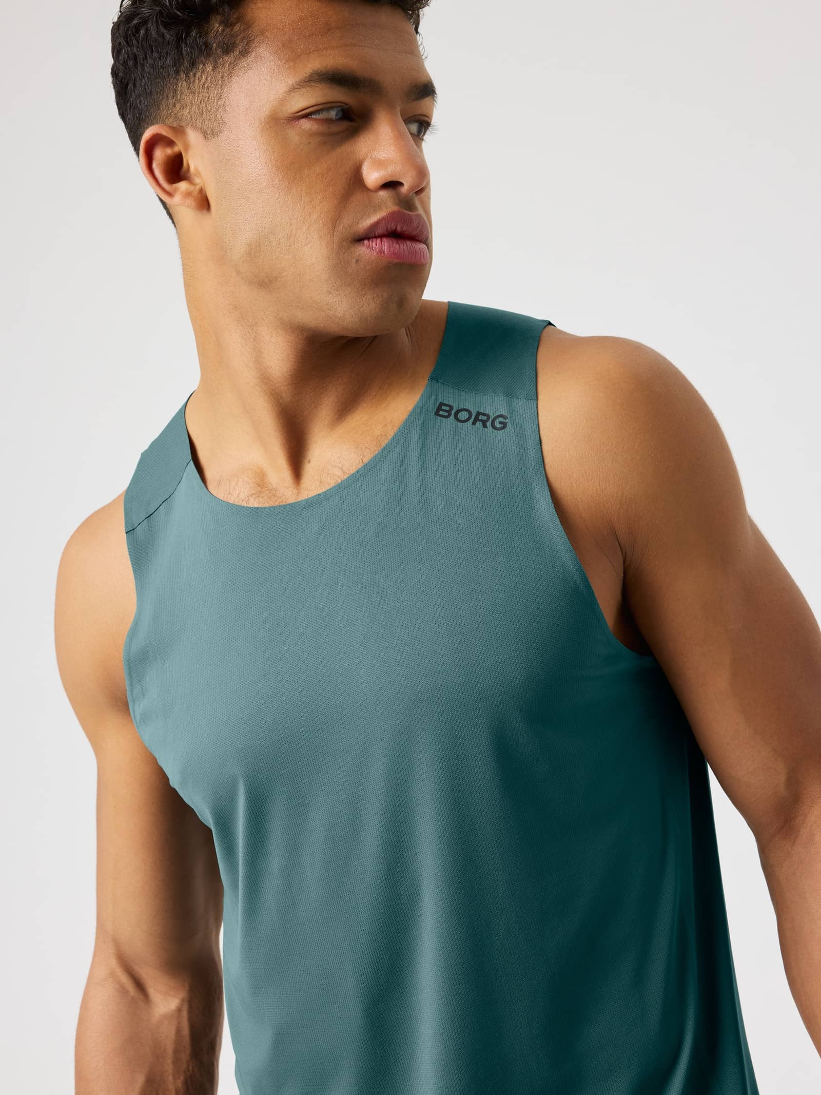 Close-up of a man wearing the Borg Feather Tank in Balsam Green (Green) with a black shoulder logo for training. - Image 1