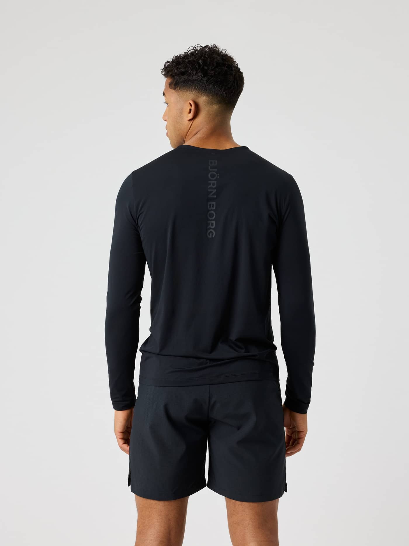 Borg Feather Long Sleeve T-Shirt i Black Beauty (Sort) set bagfra til træning og tennis med et sort logo. - Image 2