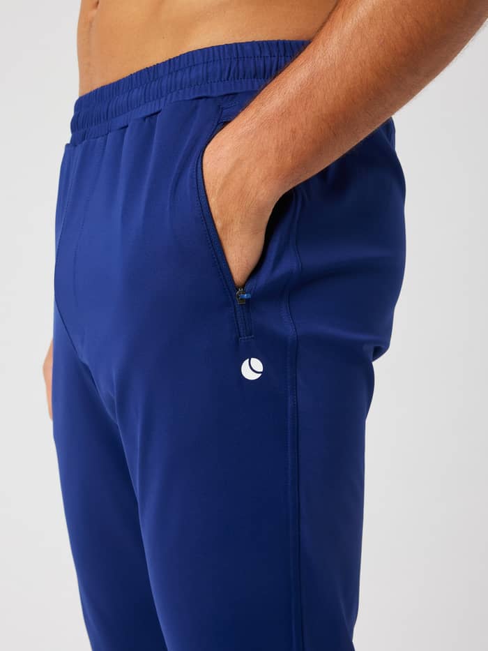 Ace Training Pants in Blue Depths (Blauw) voor heren met een ritszak en wit tennislogo, getoond in zijaanzicht. - Image 4