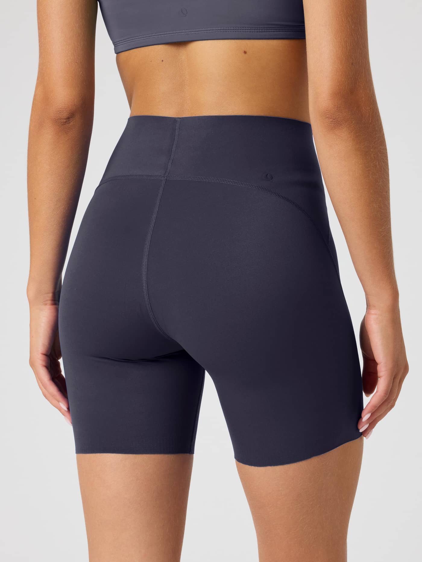 Back view of a model wearing high-waisted, slim-fit Borg Sleek Shorts in Odyssey Gray (Navy) with a tonal logo for training. - Image 2