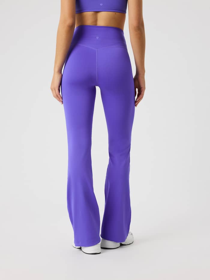 Rückansicht eines Models in Borg Flare Tights Regular in Simply Purple (Lila) mit hohem Bund und weißem Logo fürs Training. - Image 3