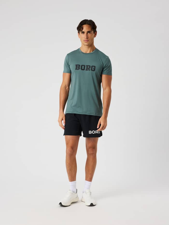 Vooraanzicht van een man in het Balsam Green (Groen) Borg Graphic T-Shirt met zwart logo voor training en tennis. - Image 4