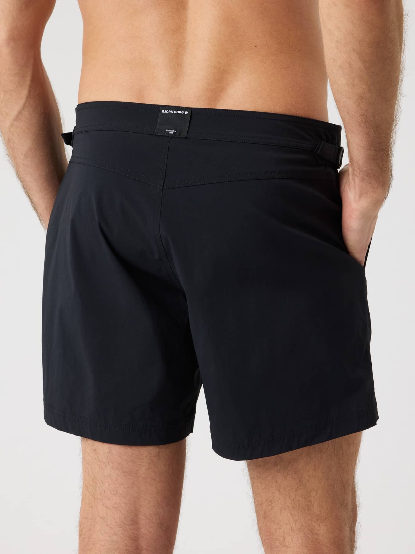 Back view of a man in the Borg Tailored Swim Shorts in Black Beauty (Black), featuring functional side buckles. - Image 2