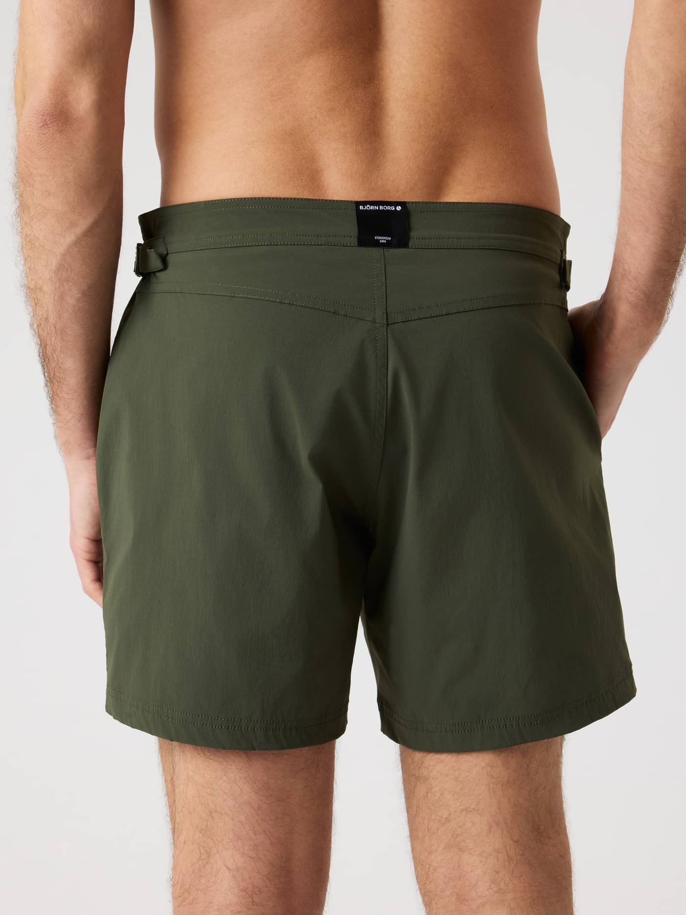 Back view of a man wearing Forest Night (Green) Borg Tailored Swim Shorts, with side buckles and a black logo label. - Image 2