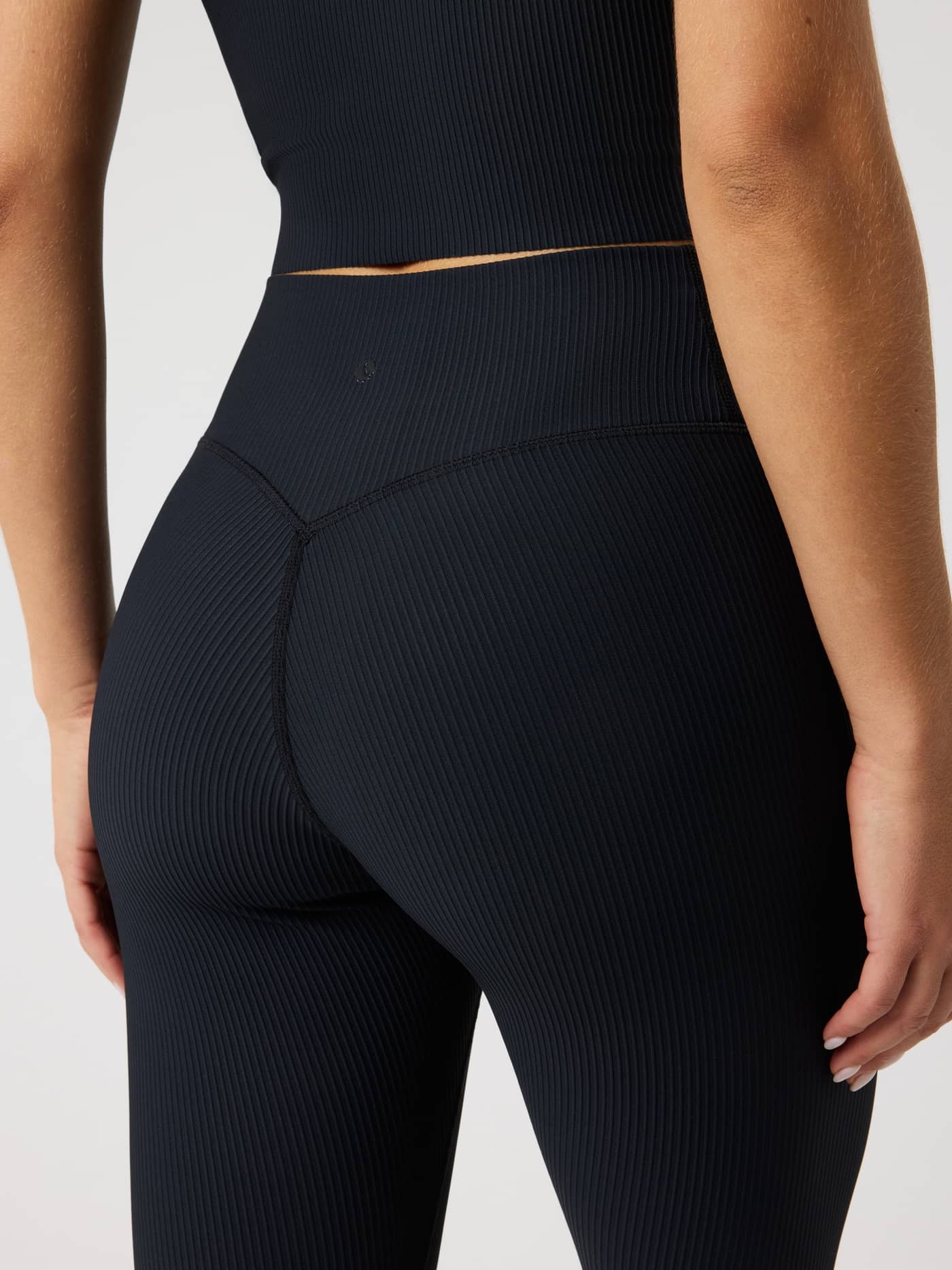 Back view of a model wearing Studio Ribbed Tights in Black Beauty (Black) with a ribbed texture and tonal logo for training. - Image 4