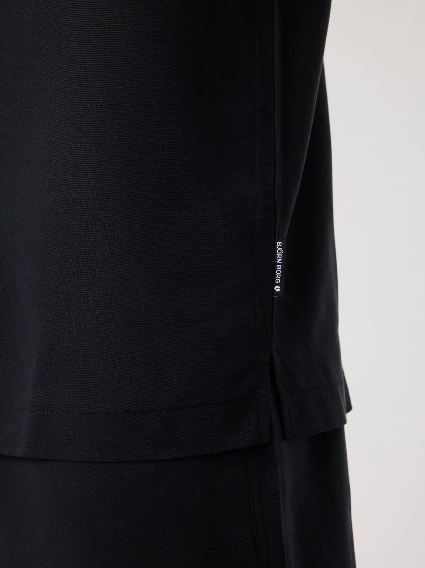 Close-up side view of the Borg Lyocell Resort Shirt in Black Beauty (Black) showing the side slit and white logo label. - Image 6