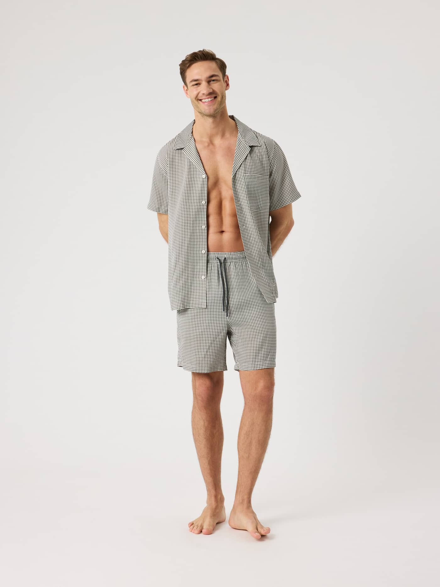 Full-body front view of a man in the regular fit Björn Borg Lyocell Resort Shirt in Houndstooth 3 (Black, White) and shorts. - Image 4
