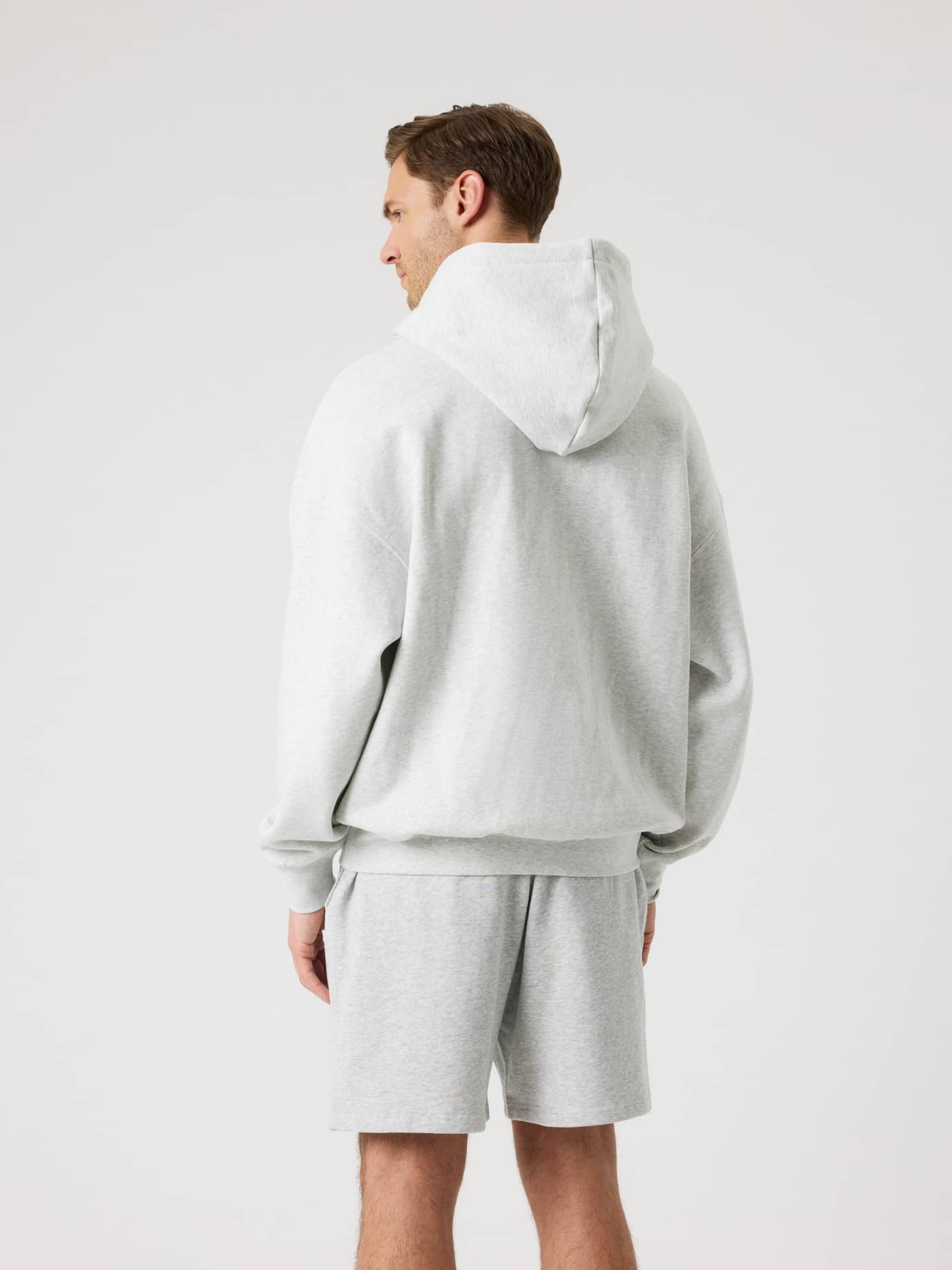 Back view of a man wearing the Borg Oversized Hoodie in Ultra Light Grey Melange (Grey) with a double layer hood. - Image 7