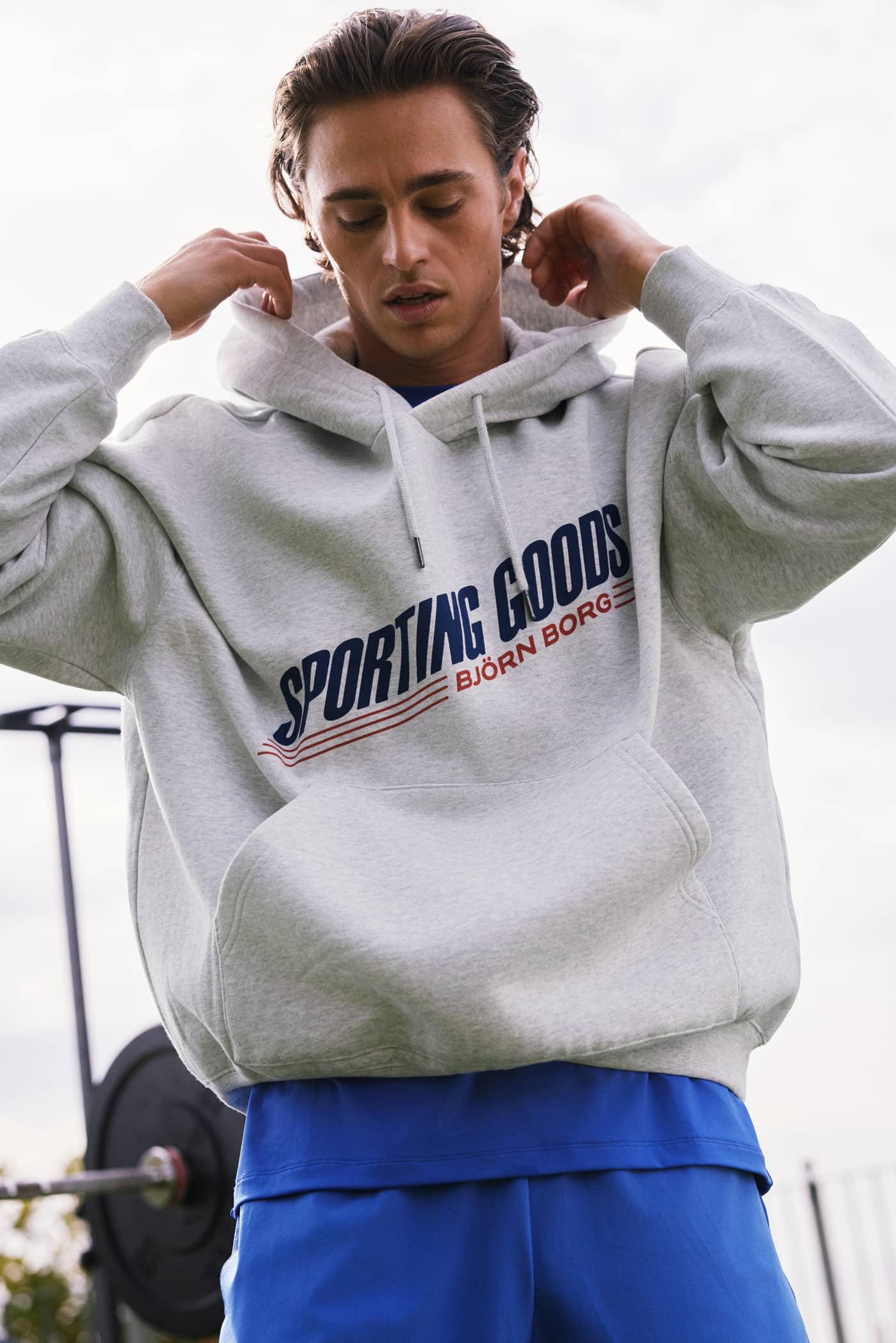 Man in the cotton Ultra Light Grey Melange (Grey) Borg Oversized Hoodie with a navy and red training chest graphic. - Image 2