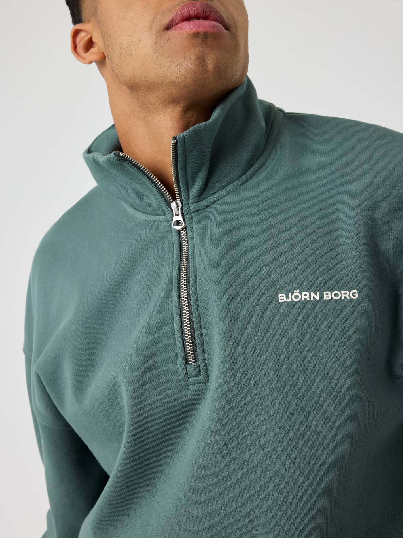 Nahaufnahme eines Mannes im Borg Oversized Half-Zip in Balsam Green (Grün) mit weißem Brustlogo und funktionalem Zip. - Image 4
