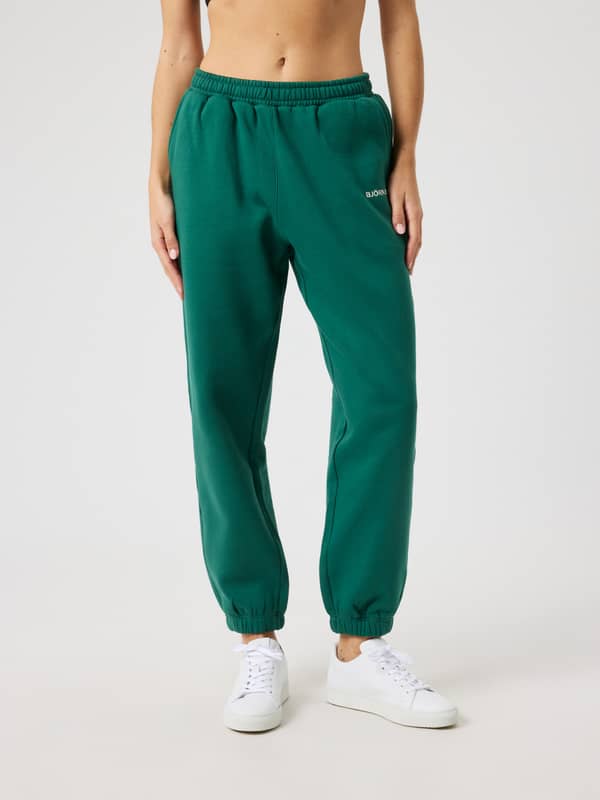 Front view of a woman in regular fit Borg Sweatpants in Posy Green (Green) with a white logo for tennis performance.