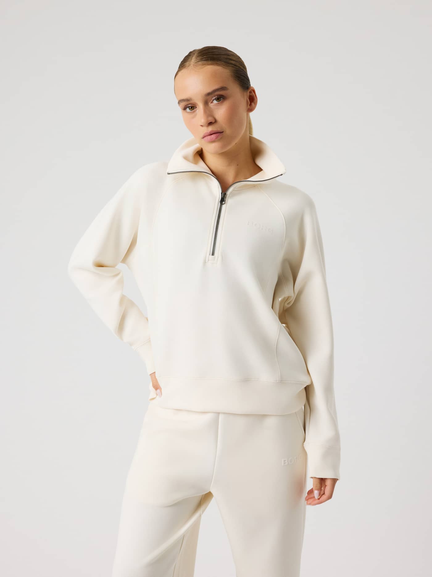 Front view of a woman wearing the Studio Soft Halfzip Sweatshirt in Tofu (White) featuring a tonal logo and loose fit. - Image 4