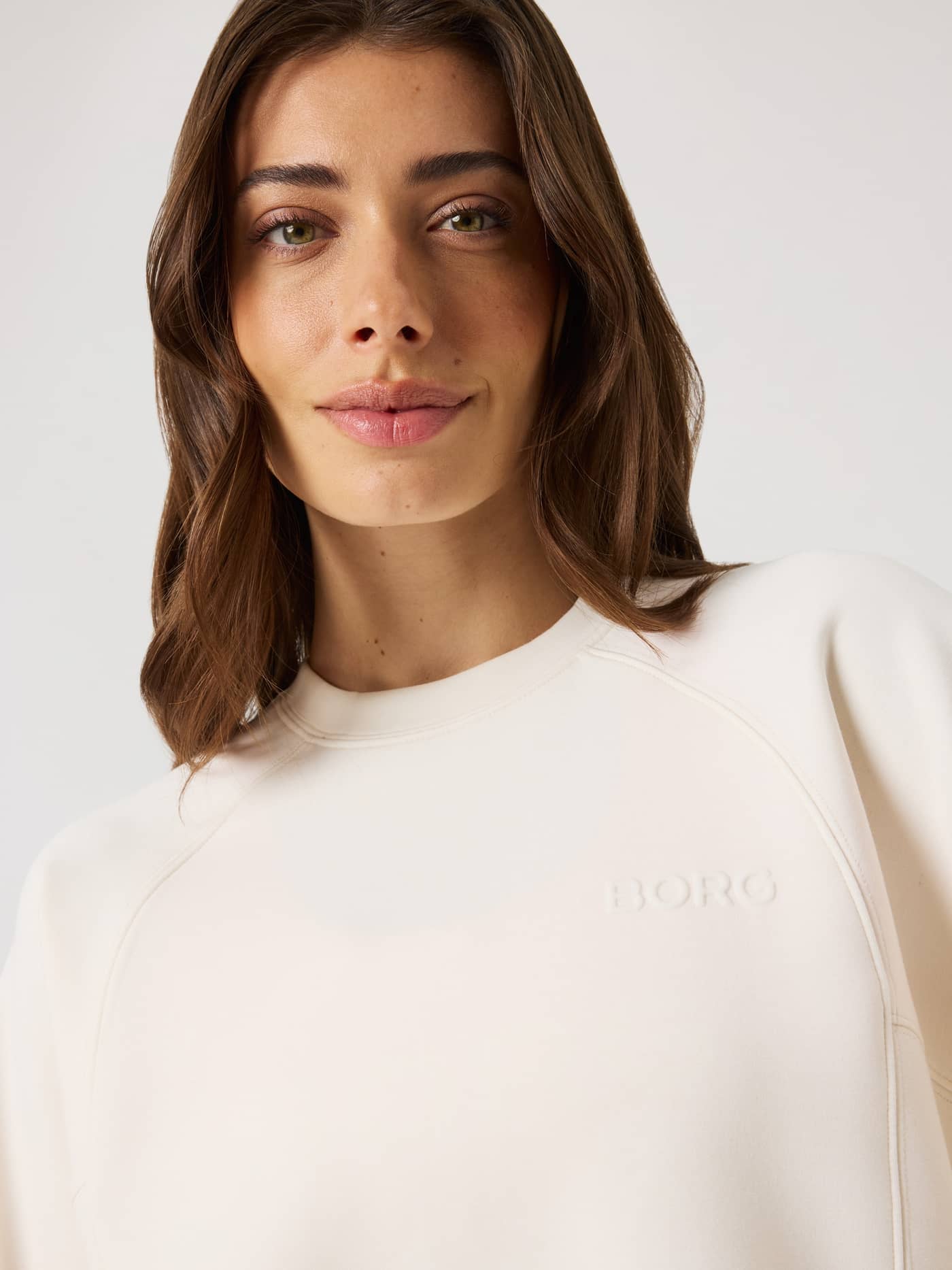 Gros plan d'une femme en Studio Soft Sweatshirt Tofu (Blanc) avec un logo BORG ton sur ton et une coupe décontractée. - Image 5