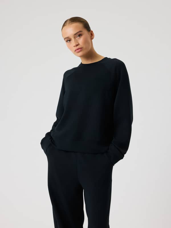 Front view of a model in the Studio Soft Sweatshirt in Black Beauty (Black), with a tonal logo and stylish, relaxed fit.