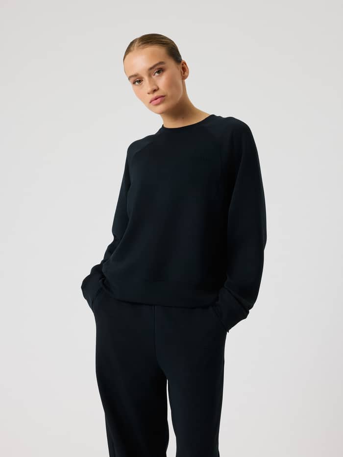 Front view of a model in the Studio Soft Sweatshirt in Black Beauty (Black), with a tonal logo and stylish, relaxed fit.