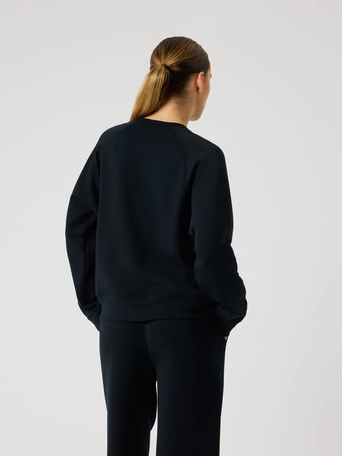 Rückansicht einer Frau im Studio Soft Sweatshirt in Black Beauty (Schwarz) mit entspannter Passform und Raglanärmeln. - Image 2