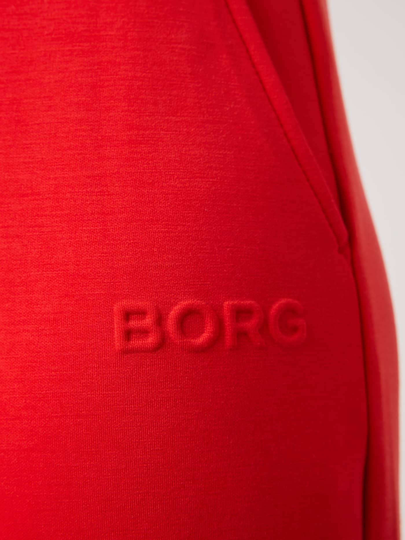 Detail of the Studio Soft Sweatpants in Flame Scarlet (Red) featuring a premium tonal embossed BORG logo. - Image 6