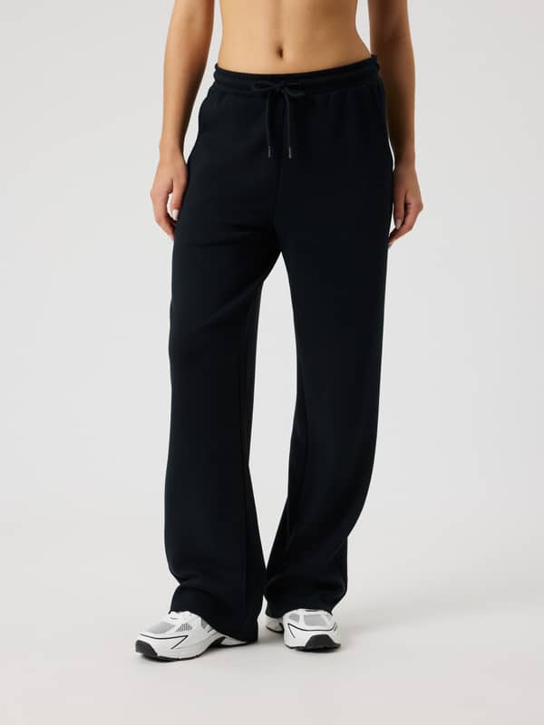Front view of a woman wearing Studio Soft Sweatpants in Black Beauty (Black) with a black logo and comfortable, relaxed fit.