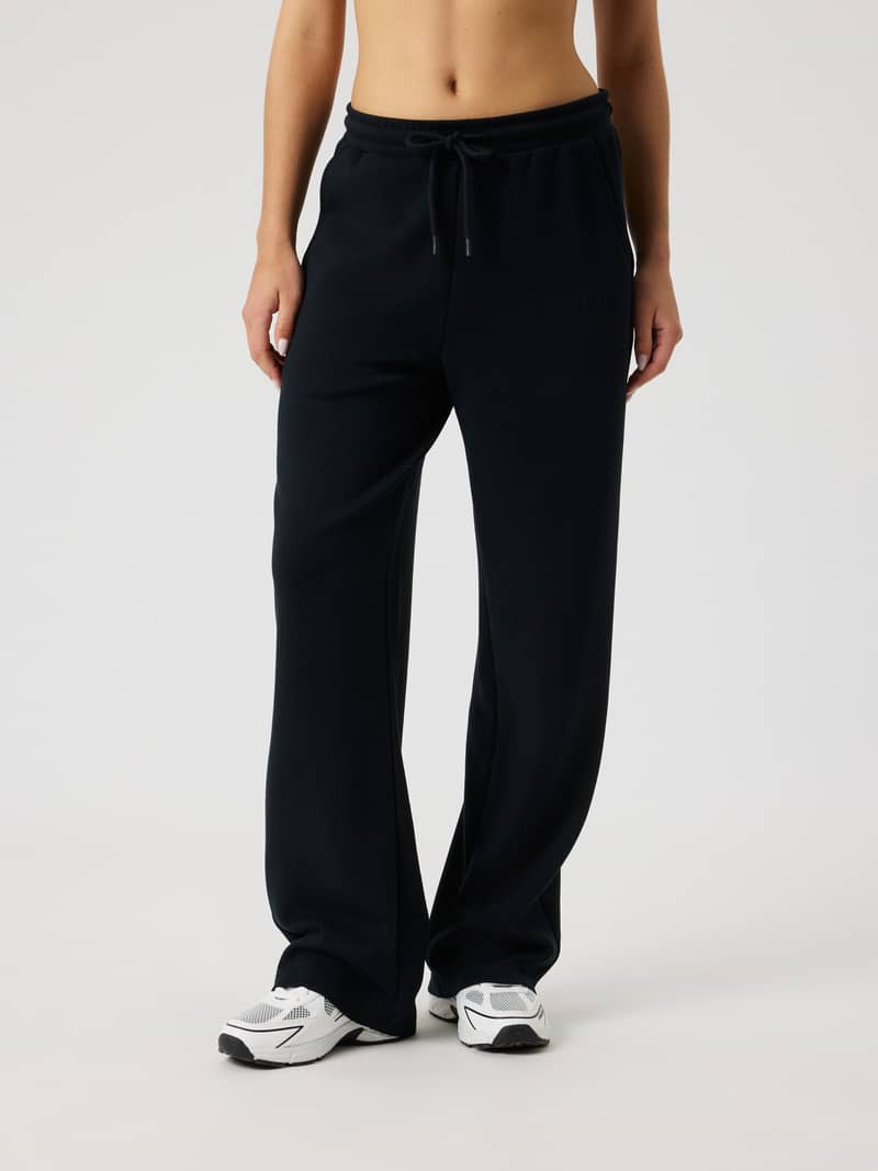 Front view of a woman wearing Studio Soft Sweatpants in Black Beauty (Black) with a black logo and comfortable, relaxed fit.