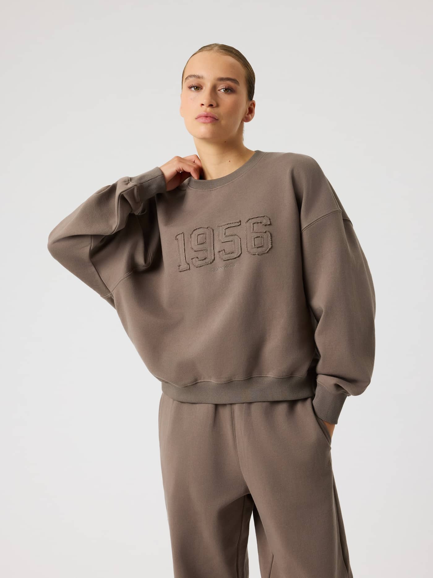 Front view of a model wearing the Studio Oversized Sweatshirt in Falcon (Brown) featuring an oversized fit and 1956 detail. - Image 2